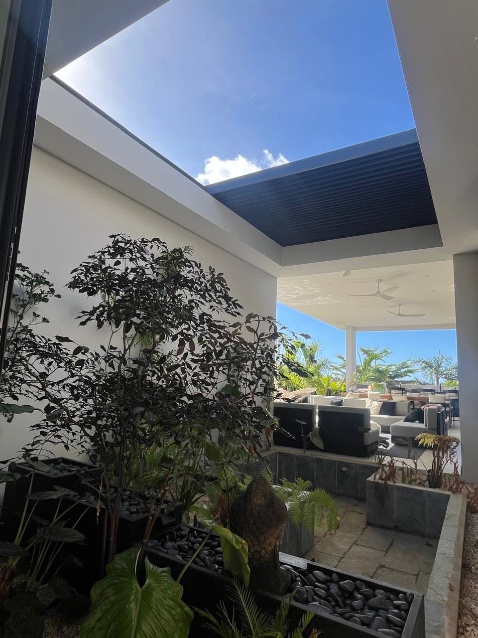 Central patio under a bioclimatic pergola with black planters and a Buddha
