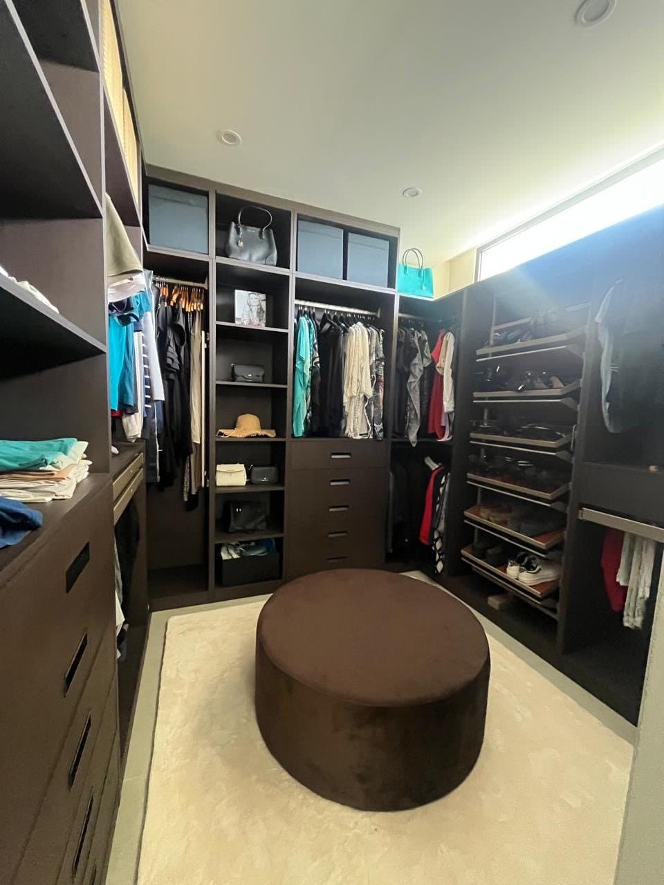 Walk-in dressing room in dark wood with velvet pouf