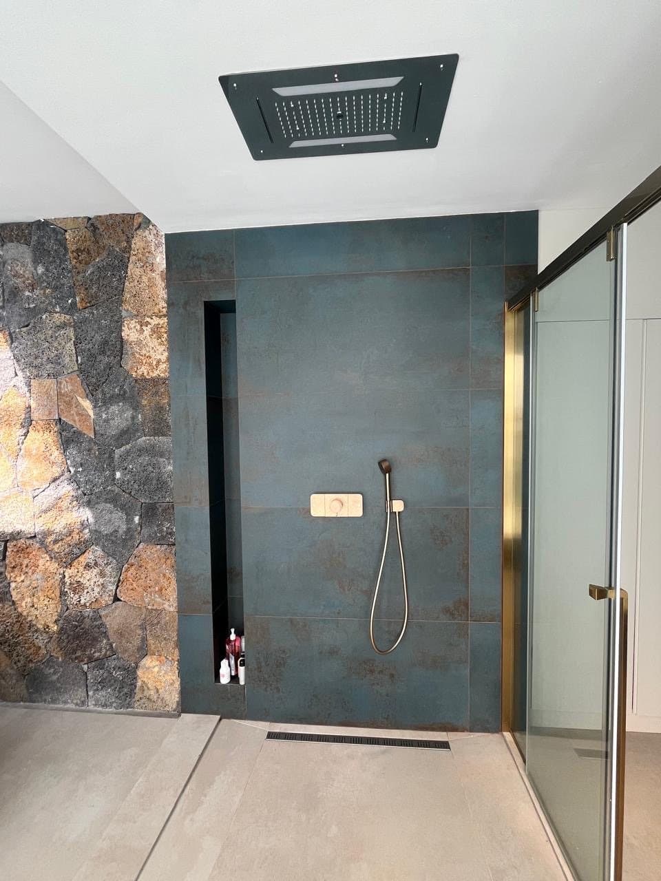Ceiling rain shower with blue steel tiles and brass glass screen