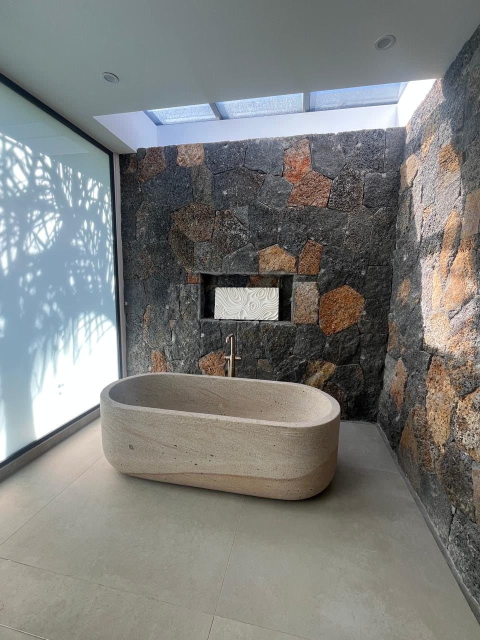 Carved stone bathtub under a skylight, volcanic stone wall