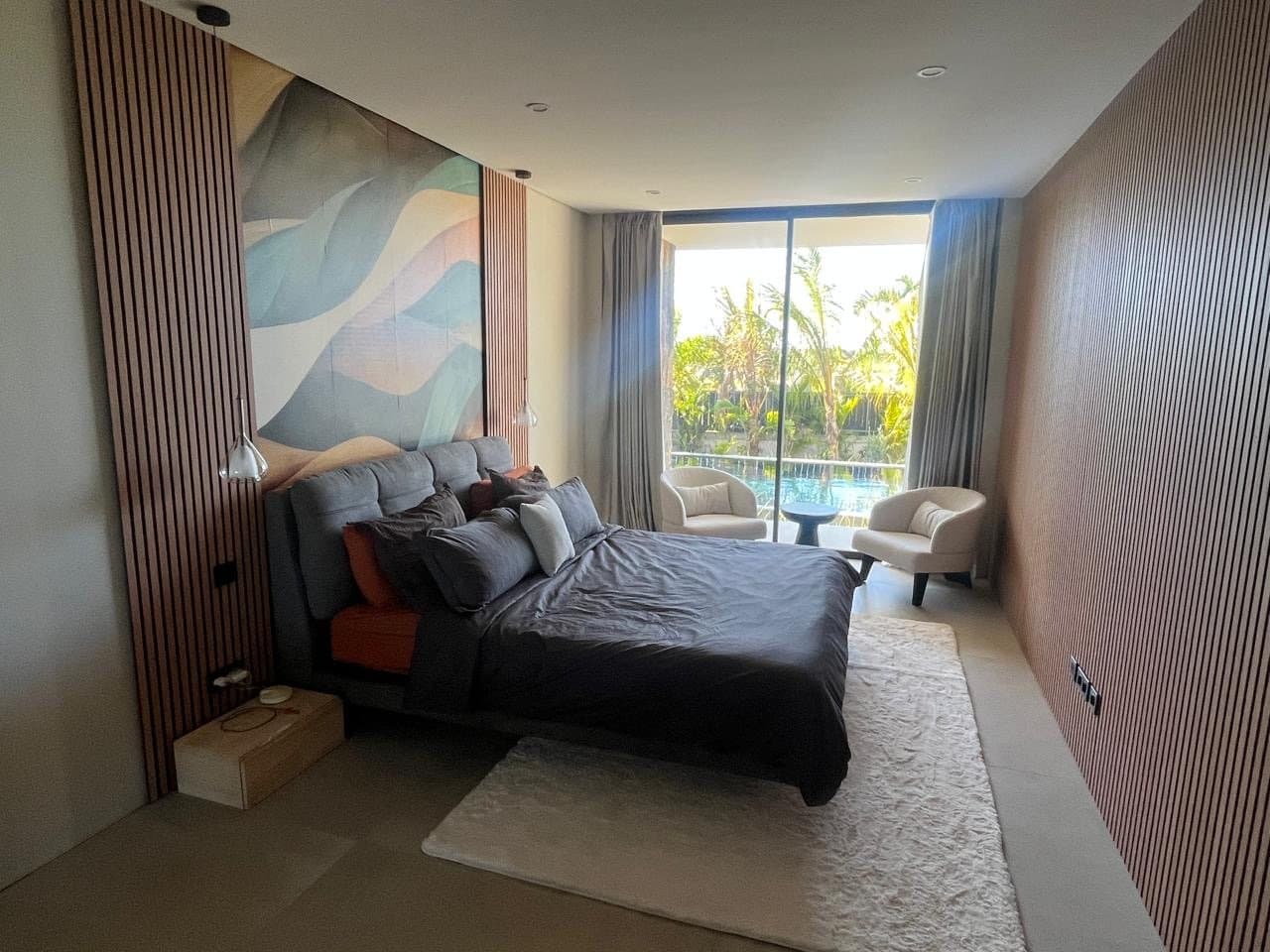 Master bedroom with cream armchairs in front of the pool-side window