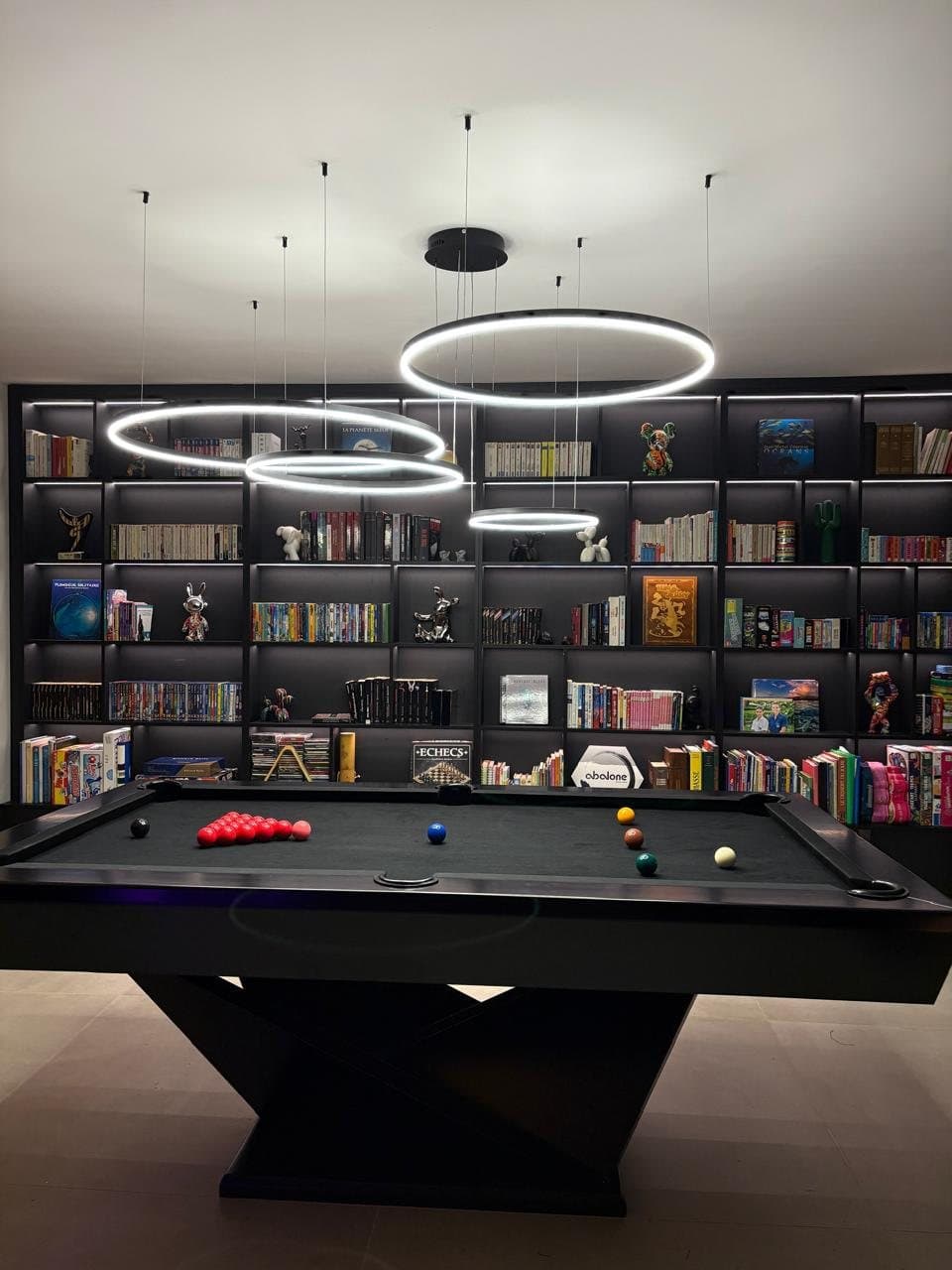Black billiard table under three LED rings, library wall behind